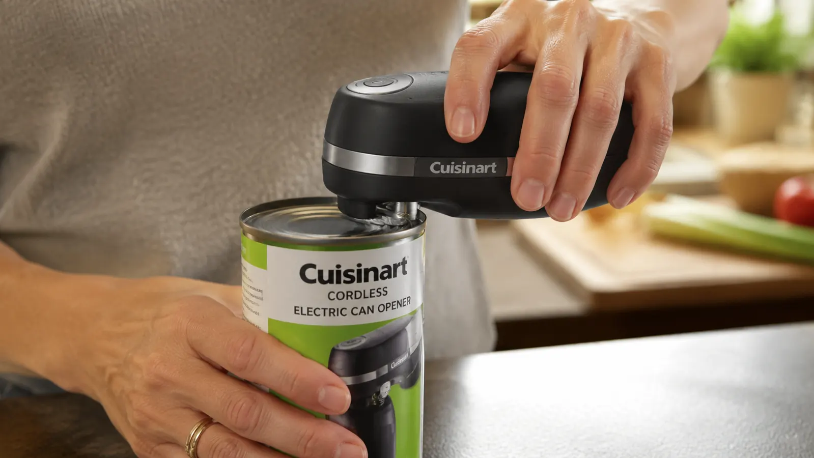Close-up of the Cuisinart can opener cutting wheel engaged on the side of a can rim, showing the smooth-edge cut in progress
