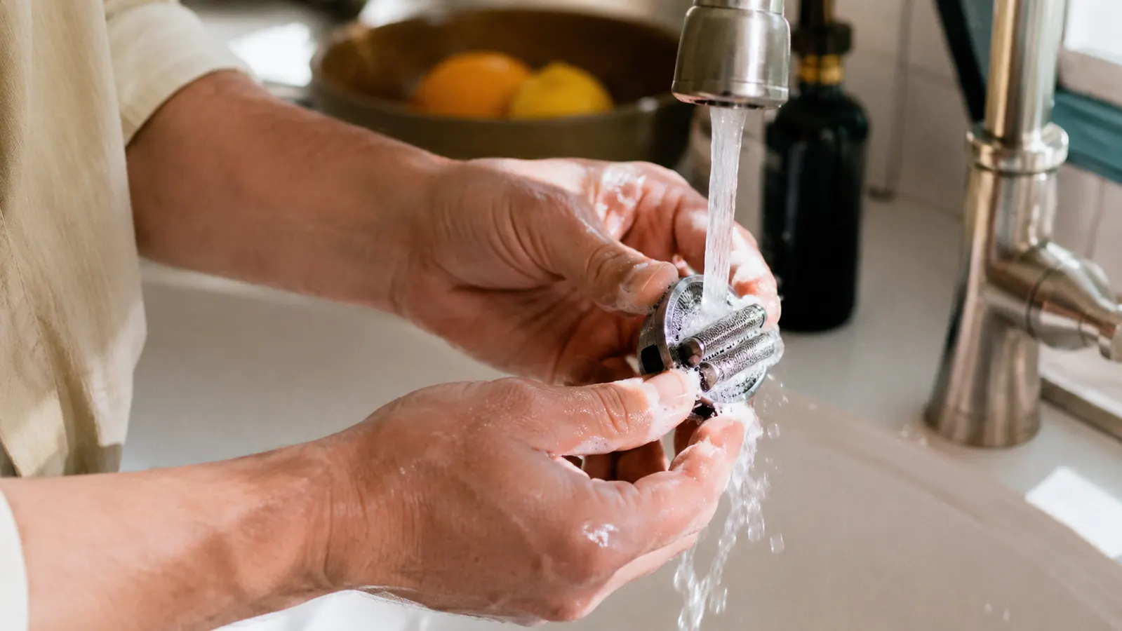 Person rinsing the detachable cutting assembly of the Cuisinart electric can opener under the faucet