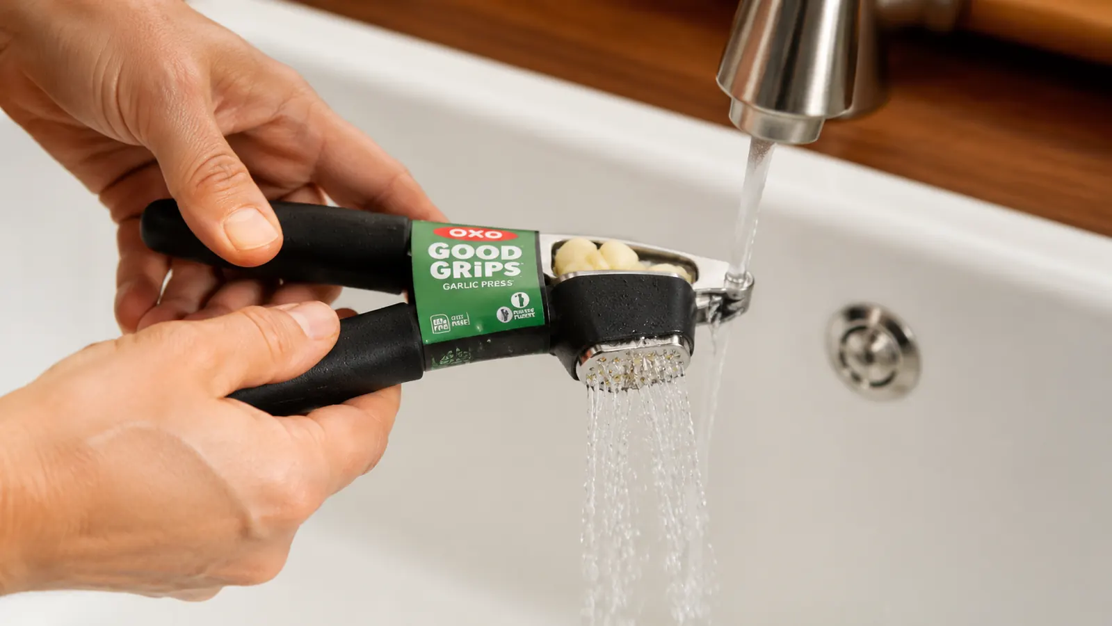 Garlic press rinsed under running water immediately after use, skins still in the chamber