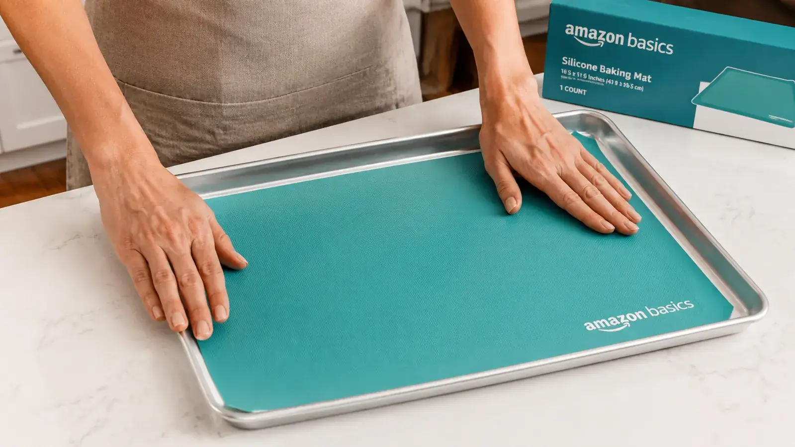 Hand placing an Amazon Basics silicone baking mat flat onto a rimmed half-sheet baking pan