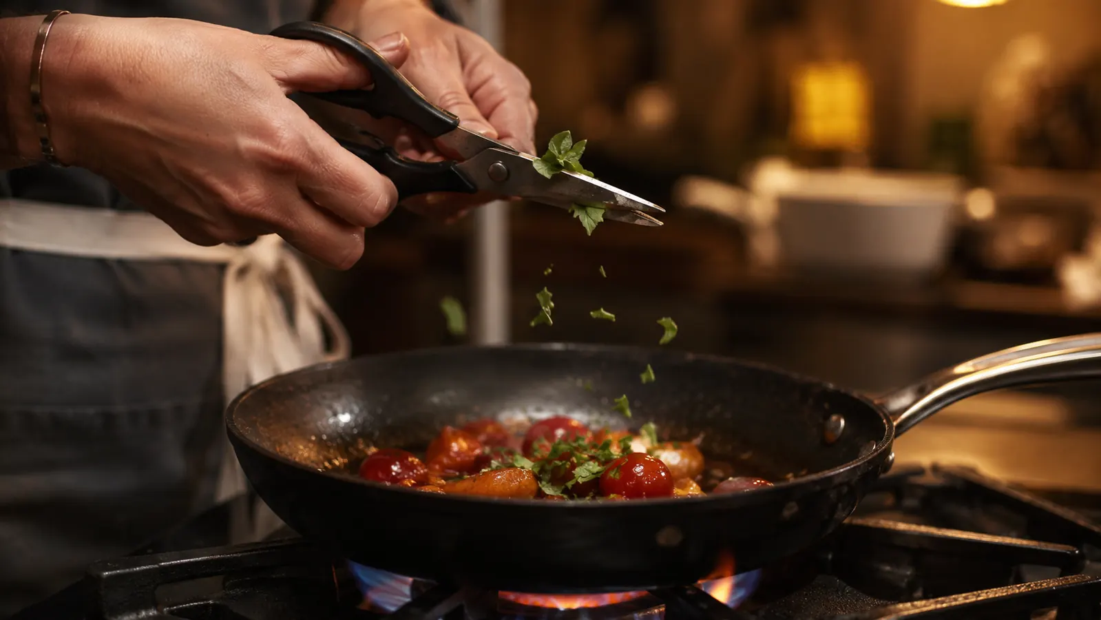Kitchen shears snipping fresh herbs directly into a skillet on a gas stove
