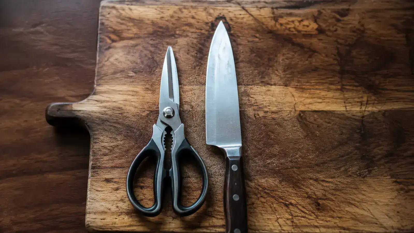 Kitchen shears and a chef's knife side by side on a wooden cutting board