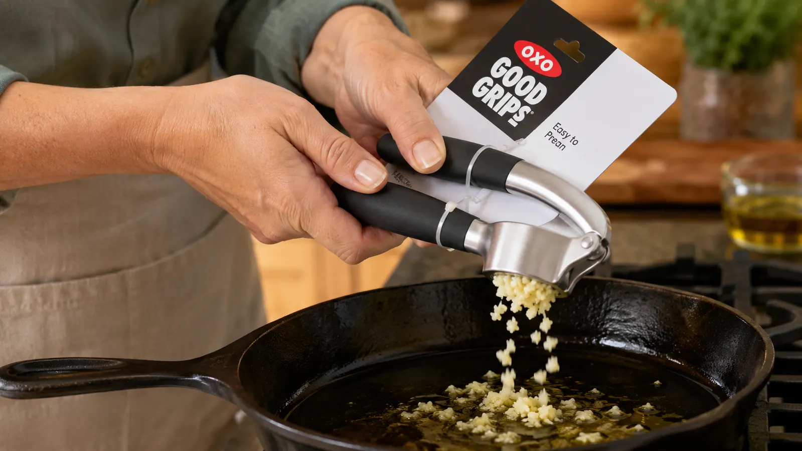 OXO Good Grips Garlic Press held over a skillet with minced garlic falling into sizzling olive oil