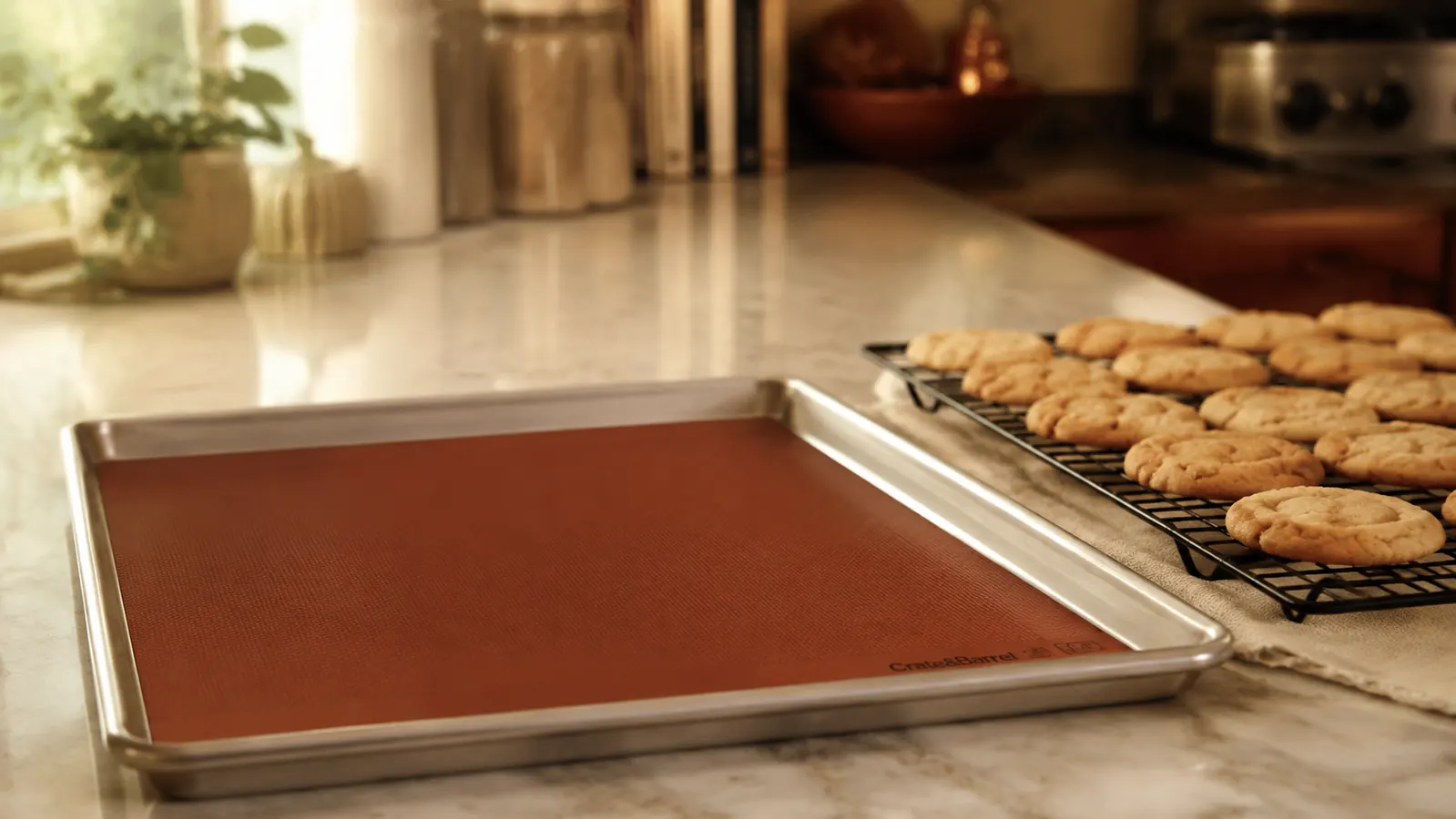 Silicone baking mat on a rimmed sheet pan resting on a kitchen counter beside a cooling rack of golden-brown sugar cookies
