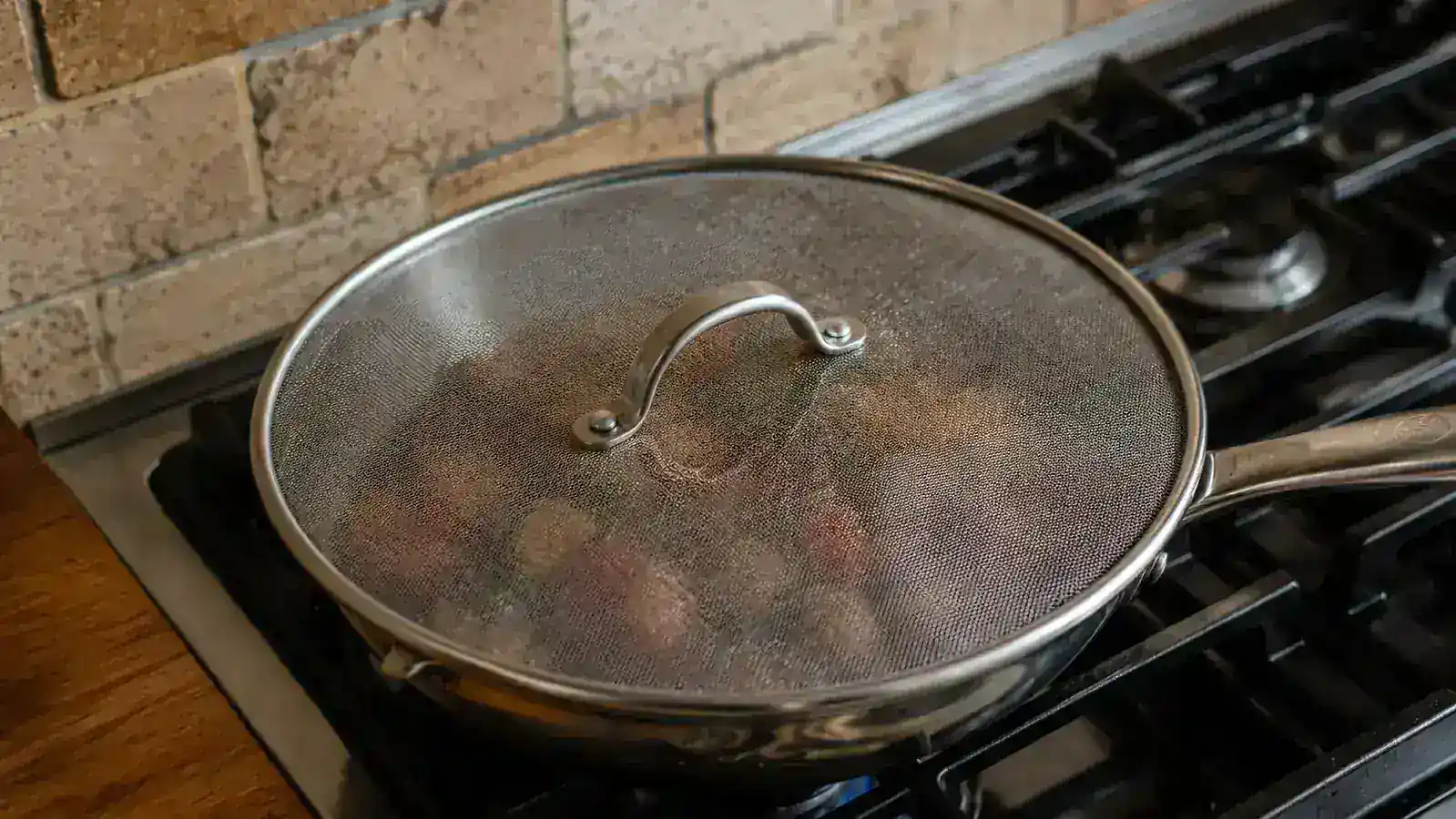 Splatter screen resting on a sauté pan over a gas stovetop burner with a kitchen towel nearby